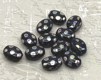Ten black oval Czech glass beads with iridescent dots scattered on a textured grey background.