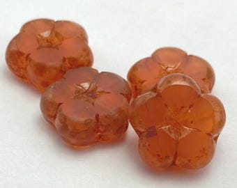 Four salmon pink Czech table cut flower beads with amber streaks and picasso finish lie on a plain white background.