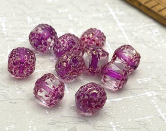 Ten purple Czech cathedral beads with rounded, bumpy surfaces and gold accents scattered on a pale textured background.