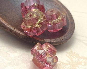 Three pink Czech glass crown beads with gold lustre on a dark wooden spoon against a cream background.