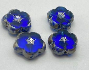Four deep blue Czech glass flower beads with metallic picasso finish and silver star details, arranged on a plain light.