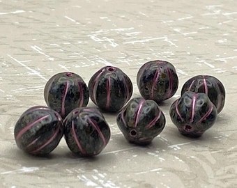 Seven black melon beads with pink wash and detailed grooves displayed on a pale textured background.