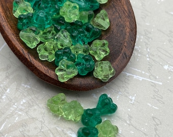 Czech glass blossom flower beads in shades of green and teal scattered on a white surface next to a wooden ruler for scale.