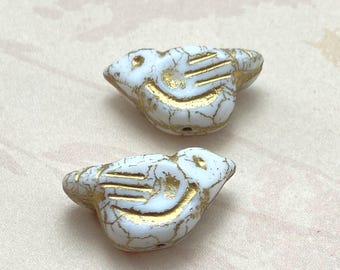 Two white Czech bird beads with gold detailing on a plain beige background, shown from the side.