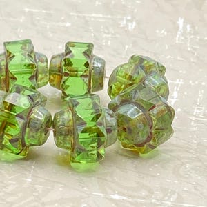 Puede incluir: Una hebra de seis cuentas de vidrio verde con un diseño facetado en forma de estrella. Las cuentas tienen un acabado ligeramente iridiscente, dorado.