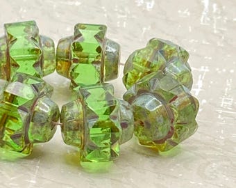 About twelve Czech glass crown beads in peridot green with Picasso finish arranged on a plain white background.