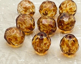Nine topaz brown Picasso Czech glass fire polished beads arranged on a pale stone background.