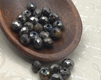 Gunmetal Czech glass rondelle beads in a wooden bowl and scattered on a pale surface, showing their faceted finish and dark.