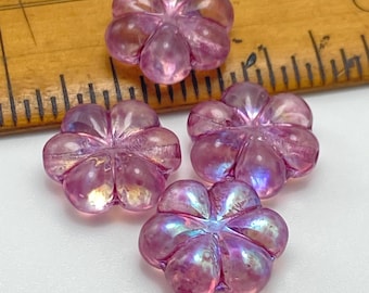 Four deep pink AB Czech glass flower beads displayed against a wooden ruler showing scale on a white surface.
