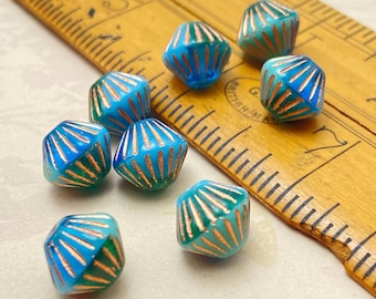 Eight turquoise blue Czech glass bicone beads with copper stripe detail scattered on and next to a wooden ruler for scale.