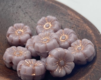 Ten pinky lilac Czech glass hibiscus flower beads with copper wash detail in a wooden bowl on white background.