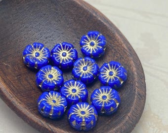 Ten opaque blue Czech glass hibiscus flower beads with gold wash detailing on a white background.