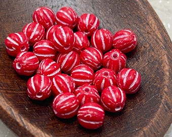 About twenty-five red Czech glass melon beads with silver-white wash arranged on a dark wooden dish.