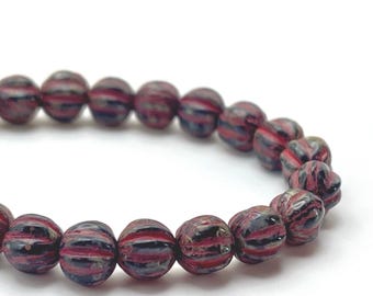 Strand of approximately twenty-five black Czech glass melon beads with red wash, arranged in a curved line on a plain.