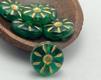 Five matte emerald green Czech glass sunflower beads with gold wash detail, displayed in a brown wooden dish and on a plain.