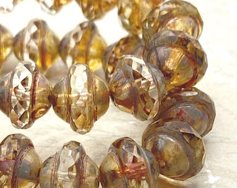 Eight Czech glass Saturn beads in clear amber with Picasso finish, showing faceted sides and disc-like shape on a pale.