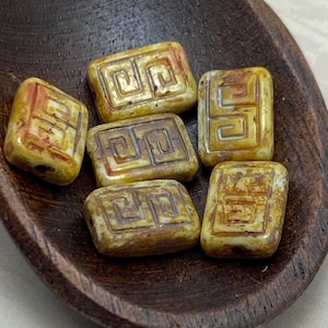 May include: Six yellow and brown ceramic tiles with a geometric pattern. The tiles are in a wooden bowl.