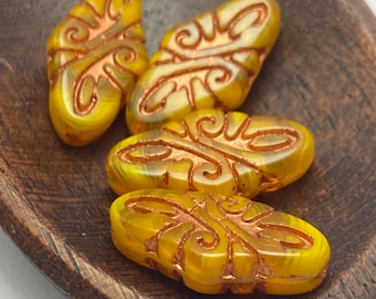 Four dandelion yellow Czech glass arabesque statement beads with copper wash detail, displayed in a wooden bowl.