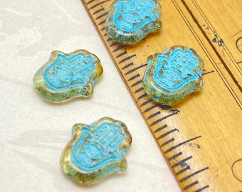 Four Czech glass hamsa hand beads in clear Picasso with turquoise wash shown next to a wooden ruler for scale.