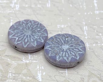 Two pale lilac coin beads with an embossed origami flower pattern, shown on a plain light background.