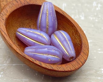 Four lilac melon drop beads with gold wash detail nestled in a wooden bowl on a plain background.