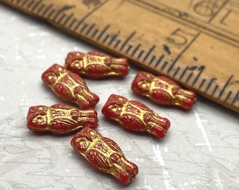 Six scarlet red Czech glass owl beads with gold wash detail displayed next to a wooden ruler for scale.