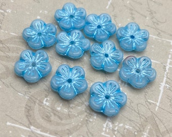 Eight pale blue Czech glass daisy beads with delicate petal details arranged on a plain textured background.