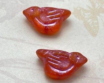 Two matte orange Czech glass bird beads with pink wash and carved detail lines, on a plain pale background.