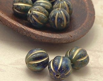 Czech glass melon beads in sapphire blue with gold wash stripes, shown in a wooden bowl and scattered on cream fabric.