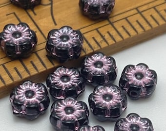 Twelve black and pink Czech glass flower beads displayed on a wooden ruler for scale.