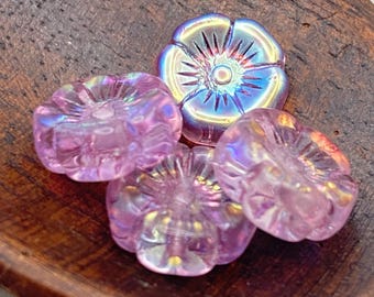 Four pink lilac Czech glass hibiscus flower beads with rainbow AB finish on a wooden dish.