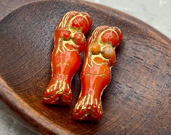 Two red mermaid tail Czech glass beads with bronze wash detail and gold highlights, resting on a wooden dish.