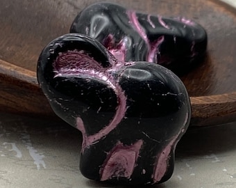 Two black Czech glass elephant beads with metallic pink wash detail, displayed on a wooden bowl.