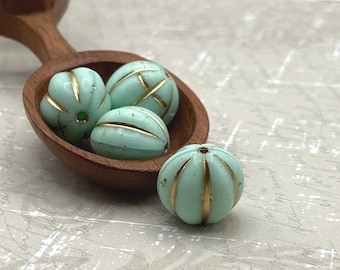 Four mint green Czech glass melon beads with gold wash stripes, three in a wooden bowl and one on a plain background.