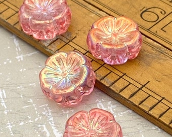 Four pink Czech glass flower beads with AB finish displayed on a wooden ruler for scale, showing their floral shape.