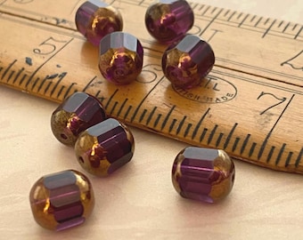 Eight purple Czech glass barrel beads with bronze finish scattered on a wooden ruler for scale.