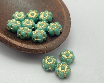 Twelve Czech glass hibiscus flower beads in turquoise with gold wash detail, displayed in a wooden bowl and on a white.