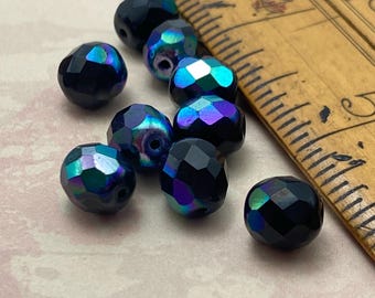 Ten jet black Czech glass faceted beads with rainbow AB coating next to a wooden ruler showing scale.