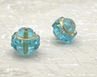Two sky blue Czech glass crown beads with gold wash and etched finish on a textured white background.