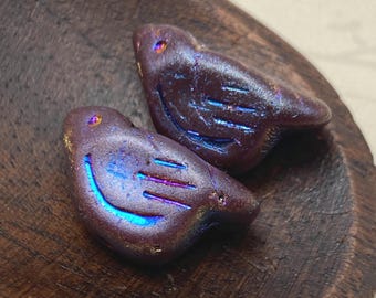 Two purple Czech glass bird beads with rainbow volcano wash detail, displayed on a wooden dish.