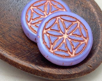 Two lilac Czech glass flower of life beads with copper wash detailing, resting in a wooden bowl.