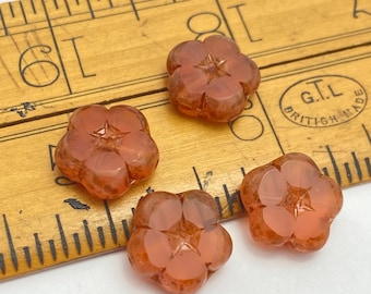 Four salmon pink Czech table cut flower beads with amber streaks and picasso finish lie on a plain white background.
