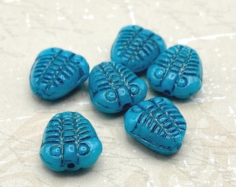 Six teal blue fossil trilobite beads with textured segmented detail on a cream speckled background.