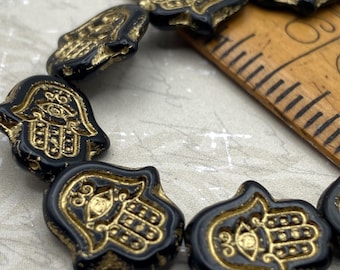 Four black Czech glass hamsa hand beads with gold wash detail arranged on a ruler against a pale background for scale.