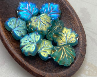 Ten teal green AB Czech glass maple leaf beads with gold wash detail, displayed in a dark wooden oval dish.