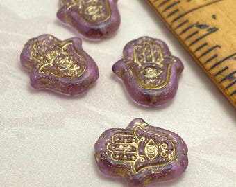 Four purple Czech glass hamsa hand beads with gold wash detail, displayed next to a ruler for scale on white background.