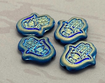 Four blue rainbow Czech glass hamsa hand beads with gold detailing on a pale background.