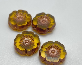 Four Czech glass hibiscus flower beads in clear yellow with ochre and copper finish on a plain grey background.