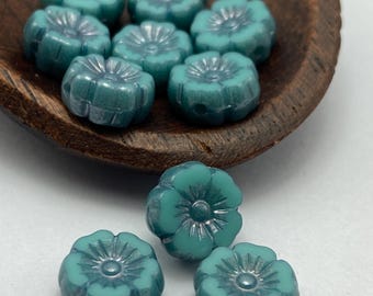 Seven teal Czech glass hibiscus flower beads in a wooden bowl with three more displayed below on a white background.