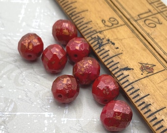 Eight deep red Czech fire polished beads with copper lustre next to a wooden ruler for scale.
